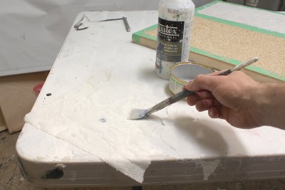 Using quilted paper towel and artist's regular clear acrylic medium, I'm going to collage torn paper towel pieces onto the oat surface.  If I can brush medium directly onto the oats, I will do that first, then apply the towel and brush more on top of that. If the oat bits are crumbling off too much for brushing them directly, I brush it onto the towel first, press it onto the oats, then brush more medium on top.  If you coat your oats with clear medium first, it makes things more fixed and will allow for easy collaging.  For the edges of the sea and around a ship, I'd use the straight edge of the towel.  For internal pieces, I make sure that they are round and torn in nature.  It doesn't matter if they over-lap.  RECENTLY, I HAVE TAKEN TO SIMPLY GLUING DOWN ONE SINGLE PIECE OF PAPER TOWEL WITH AEROSOL CONTACT CEMENT APPLIED TO BOTH SURFACES.  WAY EASIER AND NEATER